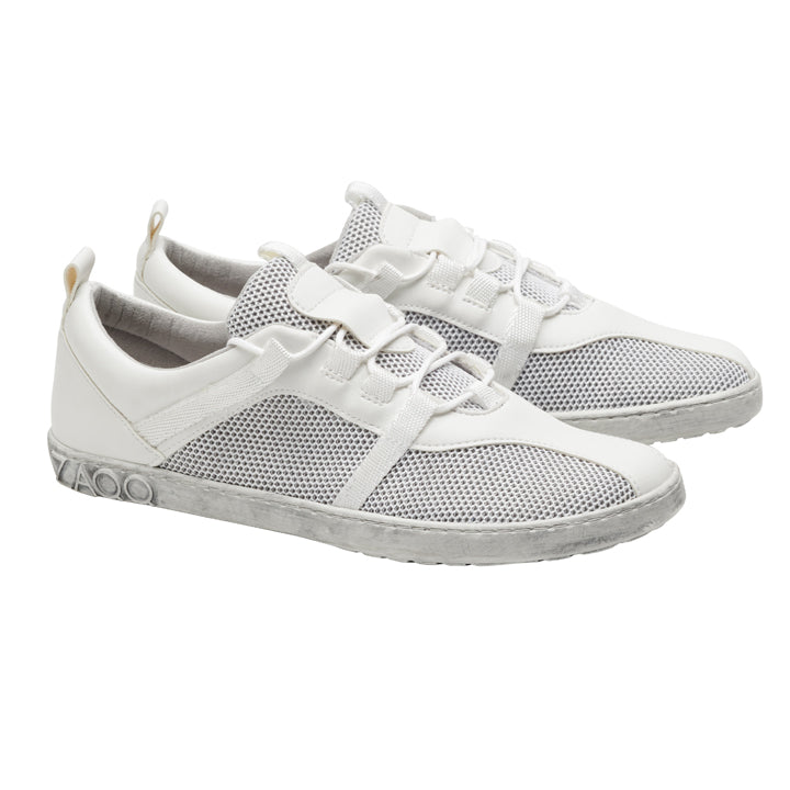 Ein Paar MCQARTER White-Sneaker von ZAQQ verfügt über atmungsaktives Meshgewebe und Schnürsenkel auf einem sauberen weißen Hintergrund, ergänzt durch eine graue Sohle mit eingeprägtem Markennamen in der Nähe der Ferse. Diese Schuhe zeichnen sich durch ein minimalistisches und sportliches Design aus.
