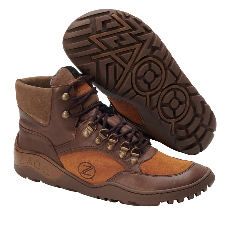 Ein Paar kamelfarbene ZAQQ TERRAQ Waterproof Wanderstiefel mit hellbraunen Akzenten. Ein Stiefel steht aufrecht und hebt das Schnürdesign mit Metallösen hervor, während der andere auf der Seite liegt und ein robustes Sohlenmuster offenbart, das perfekt für jeden Outdoor-Abenteuer ist. Das Markenlogo ist sowohl an der Seite als auch an der Sohle deutlich sichtbar.