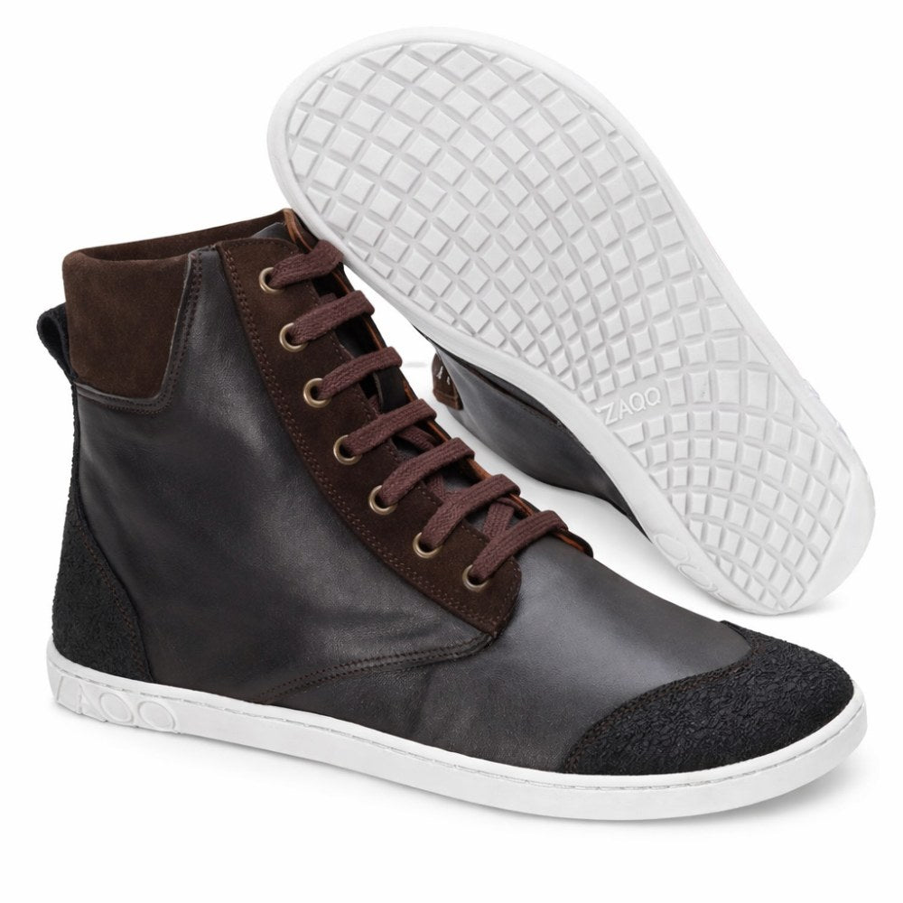 Ein Paar dunkelbraune MINSQ Mid-Cut-Sneaker von ZAQQ hat eine weiße Sohle. Ein Schuh steht aufrecht und zeigt sein Ledermaterial und die braunen Schnürsenkel, während der andere schräg steht und die strukturierte Sohle zeigt. Das Logo der Marke ist auf der Sohle sichtbar und unterstreicht das stilvolle Design.