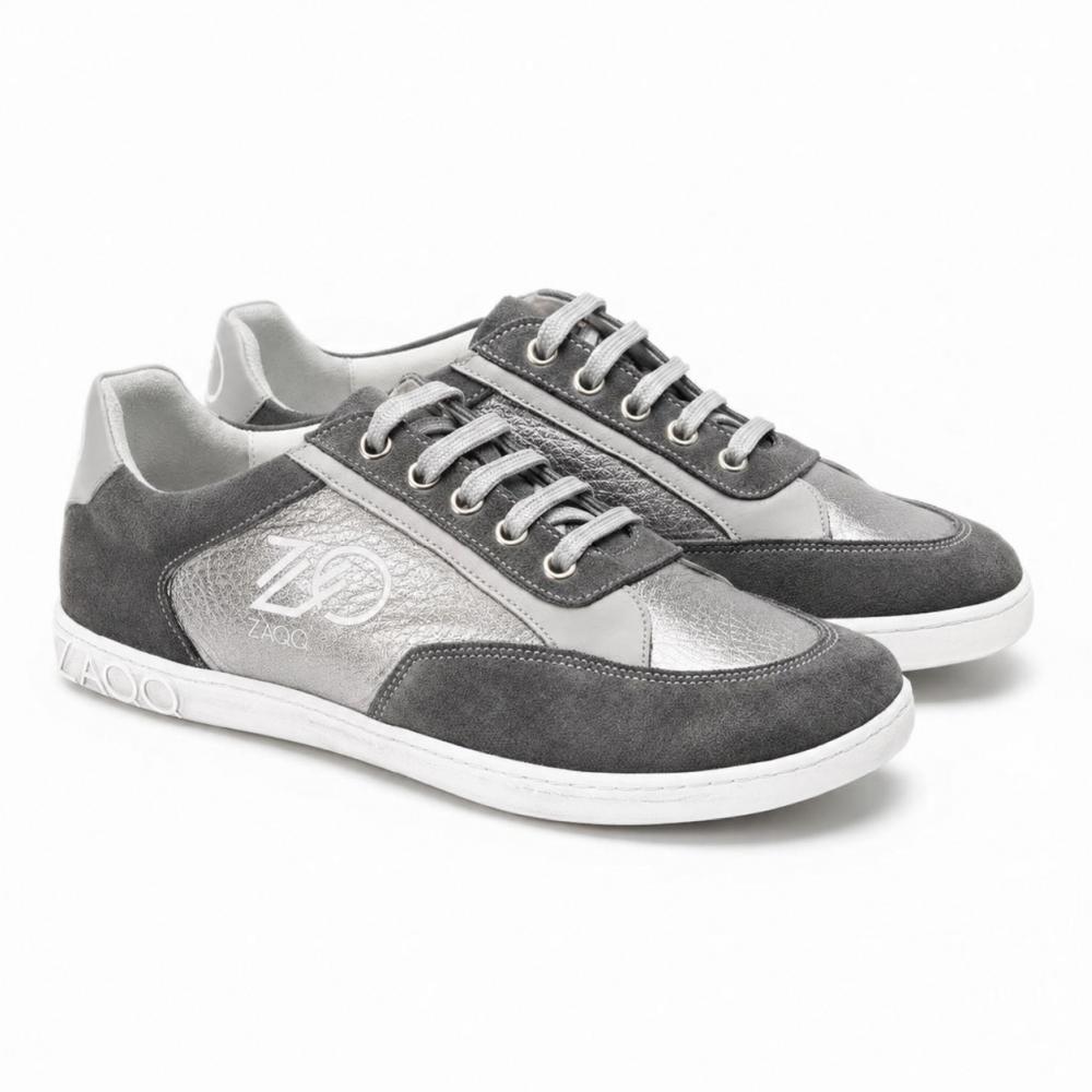 Une paire de baskets OQTAV Grey de ZAQQ, fabriquées en daim velouté et avec des empiècements texturés. Avec des lacets argentés et le logo distinctif Zagoo sur le côté et le talon, ces chaussures élégantes sont présentées côte à côte sur un fond blanc.