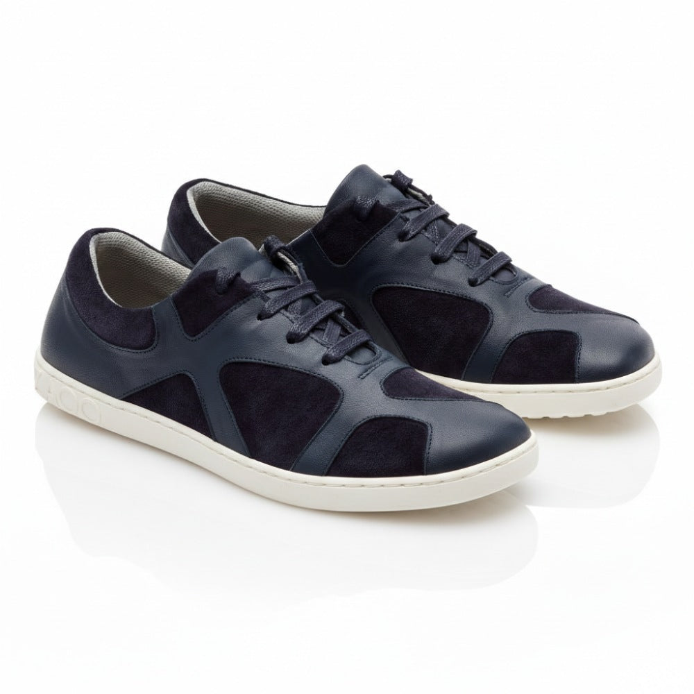 Die QAANAAQ Blue Sneaker von ZAQQ sind aus dunkelblauem Leder und Veloursleder gefertigt, haben weiße Sohlen und einen Schnürverschluss im lässigen Design. Sie bestehen aus atmungsaktivem Material und stehen auf einer weißen reflektierenden Oberfläche.