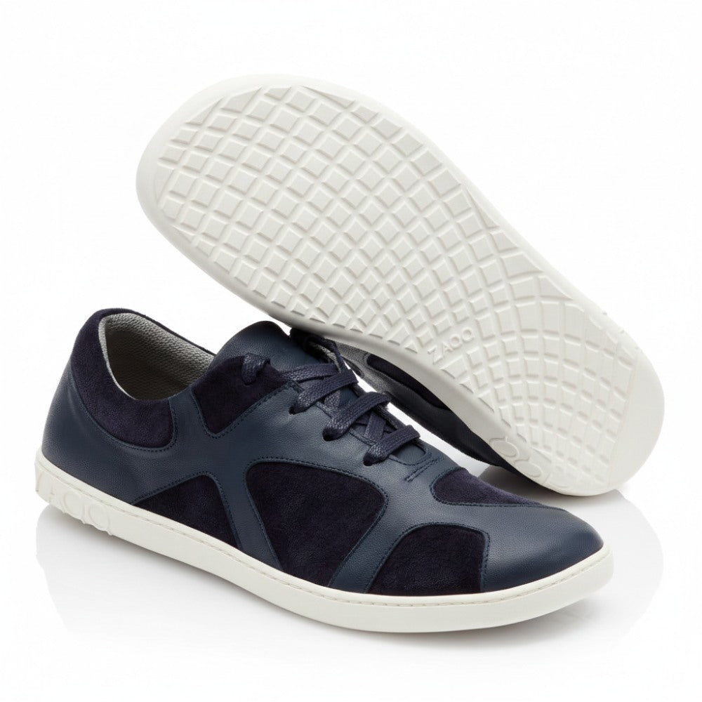 Ein Paar marineblaue Sneaker, bekannt als QAANAAQ Blue und aus atmungsaktivem Material mit grauen Sohlen, wird auf weißem Hintergrund präsentiert. Ein Schuh steht aufrecht und zeigt die Seiten- und Draufsicht, während der andere die strukturierte Sohle zeigt und den Markennamen ZAQQ trägt.