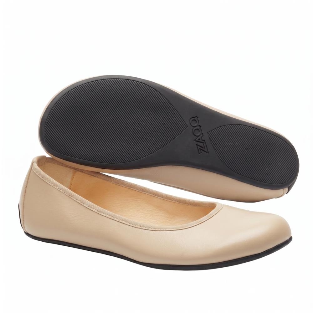 Ein Paar QARMA Beige Flats von ZAQQ hat ein beiges Obermaterial aus Nappaleder mit schwarzen Sohlen. Ein Schuh steht aufrecht und betont seine glatte Oberfläche, während der andere geneigt ist, um die strukturierte Sohle zu präsentieren.