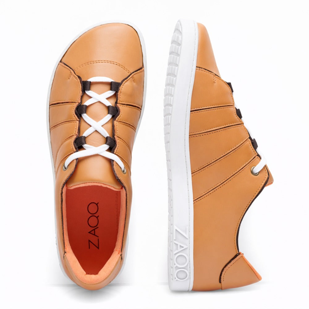 Der QQQ Low Sierra von ZAQQ ist ein Paar hellbraune Leder-Sneaker aus geschmeidigem Nappaleder. Von oben und von der Seite betrachtet, verfügen diese Sneaker über weiße Schnürsenkel und eine dicke, flexible Kautschuksohle mit dem seitlich sichtbaren ZAQQ-Branding. Die Schuhe zeichnen sich durch ein schlankes Design mit auffälligen Nähten aus.