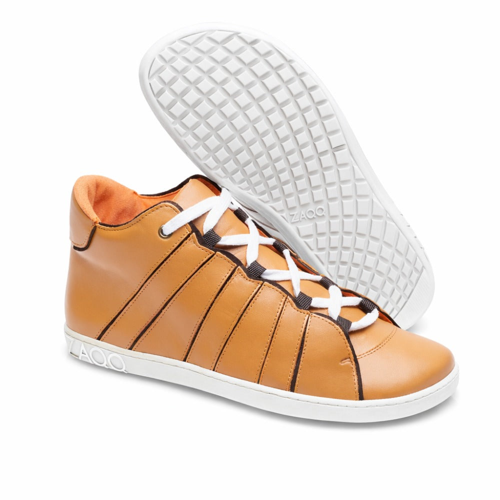 Der QQQ Mid Sierra von ZAQQ ist ein Paar High-Top-Sneaker in Braun, hergestellt aus hochwertigem Nappaleder. Sie verfügen über weiße Schnürsenkel und Sohlen; ein Schuh steht aufrecht, während der andere dagegen lehnt und das Profilmuster hervorhebt. Der Markenname ZAQQ ziert sowohl die Seite als auch die Sohle und vermittelt ein angenehmes barfußähnliches Tragegefühl.