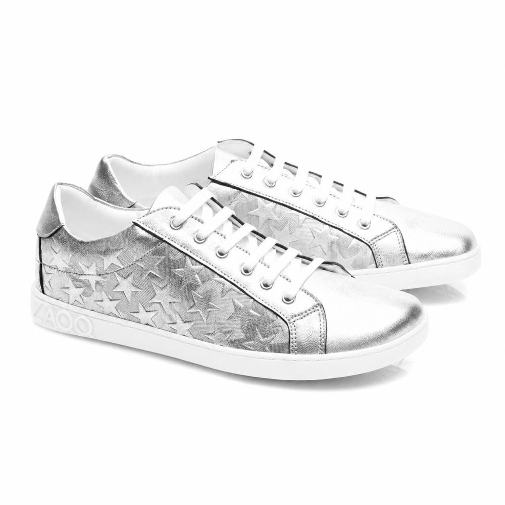Les baskets SLOQ Stars Silver de ZAQQ ont des lacets blancs et un motif étoilé sur les côtés, complétés par une semelle blanche avec l'inscription VAOO sur le talon. Ces chaussures se distinguent par un design élégant et moderne avec une finition métallique brillante.