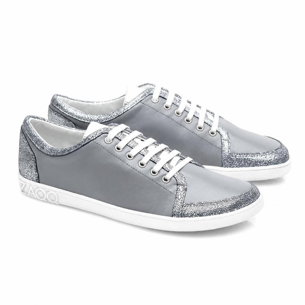 Les baskets TIQQ Grey Silver de ZAQQ se distinguent par leur design épuré en cuir nappa souple avec des lacets blancs et des accents pailletés argentés, complétés par des semelles blanches et un logo discret sur le talon, offrant le parfait mélange de style et de confort pour chaque occasion.