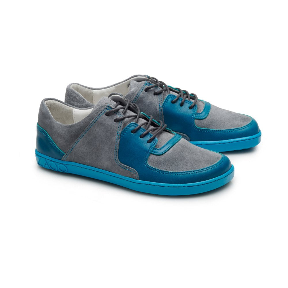 Entdecken Sie den modischen ZAQQ-Sneaker aus grauem Wildleder mit blauen Lederakzenten, ergänzt durch türkisfarbene IVIQ-Sohlen und Schnürsenkel, alles auf einem makellosen weißen Hintergrund für ein elegantes und modernes Erscheinungsbild.